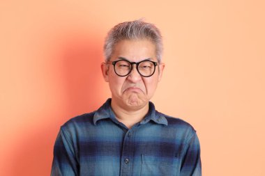 Yeşil ekose elbiseli Asyalı son sınıf öğrencisi gözlük takıyor ve turuncu arka planda öfkeli ve çığlıklar atıyor. Turist, akıllı gündelik.