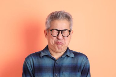 Yeşil ekose elbiseli Asyalı son sınıf öğrencisi. Gözlük takıyor. Hayal kırıklığı jesti, turuncu arka planda yalnız başına ağlıyor. Turist, akıllı gündelik.