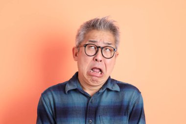 Yeşil ekose elbiseli Asyalı son sınıf öğrencisi. Gözlük takıyor ve gülüyor. Turuncu arka planda komik bir şekilde izole edilmiş. Turist, akıllı gündelik.