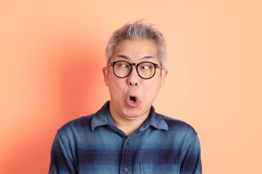 Yeşil ekose elbiseli Asyalı son sınıf öğrencisi. Gözlük takıyor ve gülüyor. Turuncu arka planda komik bir şekilde izole edilmiş. Turist, akıllı gündelik.