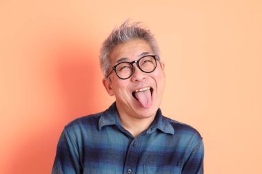 Yeşil ekose elbiseli Asyalı son sınıf öğrencisi. Gözlük takıyor ve gülüyor. Turuncu arka planda komik bir şekilde izole edilmiş. Turist, akıllı gündelik.