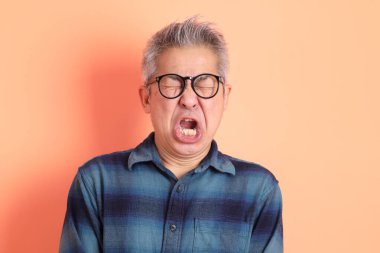 Yeşil ekose elbiseli Asyalı son sınıf öğrencisi. Gözlük takıyor. Hayal kırıklığı jesti, turuncu arka planda yalnız başına ağlıyor. Turist, akıllı gündelik.