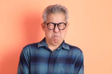 Yeşil ekose elbiseli Asyalı son sınıf öğrencisi. Gözlük takıyor. Hayal kırıklığı jesti, turuncu arka planda yalnız başına ağlıyor. Turist, akıllı gündelik.