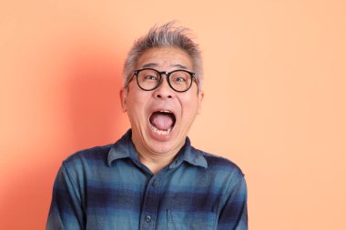 Yeşil ekose giysili Asyalı son sınıf öğrencisi gözlüklü, sürpriz jestli ve turuncu arka planda etkileyici izole edilmiş. Turist, akıllı gündelik.