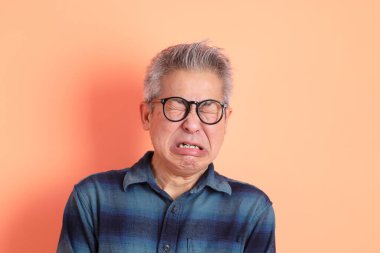 Yeşil ekose elbiseli Asyalı son sınıf öğrencisi. Gözlük takıyor. Hayal kırıklığı jesti, turuncu arka planda yalnız başına ağlıyor. Turist, akıllı gündelik.