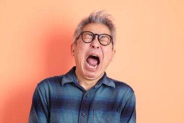 Yeşil ekose elbiseli Asyalı son sınıf öğrencisi. Gözlük takıyor. Hayal kırıklığı jesti, turuncu arka planda yalnız başına ağlıyor. Turist, akıllı gündelik.