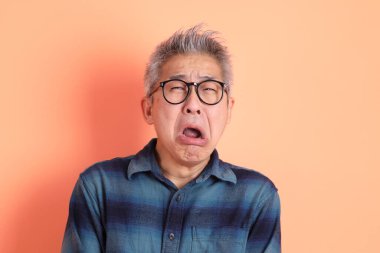 Yeşil ekose elbiseli Asyalı son sınıf öğrencisi. Gözlük takıyor. Hayal kırıklığı jesti, turuncu arka planda yalnız başına ağlıyor. Turist, akıllı gündelik.