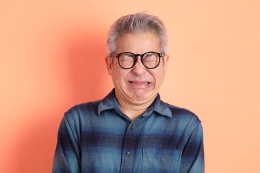 Yeşil ekose elbiseli Asyalı son sınıf öğrencisi. Gözlük takıyor. Hayal kırıklığı jesti, turuncu arka planda yalnız başına ağlıyor. Turist, akıllı gündelik.