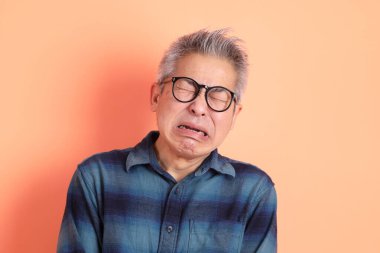 Yeşil ekose elbiseli Asyalı son sınıf öğrencisi. Gözlük takıyor. Hayal kırıklığı jesti, turuncu arka planda yalnız başına ağlıyor. Turist, akıllı gündelik.