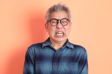 Yeşil ekose elbiseli Asyalı son sınıf öğrencisi gözlük takıyor ve turuncu arka planda öfkeli ve çığlıklar atıyor. Turist, akıllı gündelik.