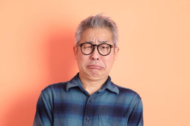 Yeşil ekose elbiseli Asyalı son sınıf öğrencisi. Gözlük takıyor. Hayal kırıklığı jesti, turuncu arka planda yalnız başına ağlıyor. Turist, akıllı gündelik.