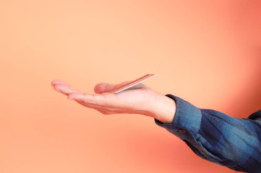 Yeşil ekose elbiseli Asyalı son sınıf öğrencisi gözlük takıyor ve turuncu arka planda kredi kartı taşıyor. Turist, akıllı gündelik.