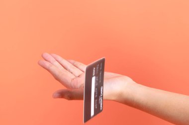 Yeşil ekose elbiseli Asyalı son sınıf öğrencisi gözlük takıyor ve turuncu arka planda kredi kartı taşıyor. Turist, akıllı gündelik.