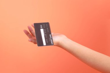 Yeşil ekose elbiseli Asyalı son sınıf öğrencisi gözlük takıyor ve turuncu arka planda kredi kartı taşıyor. Turist, akıllı gündelik.