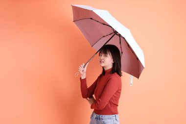 Kırmızı uzun kollu tişörtlü kısa saçlı Asyalı kadın. El ele tutuşurken mavi ve pembe şemsiyeli jest turuncu arka planda izole edilmiş. Gen Z