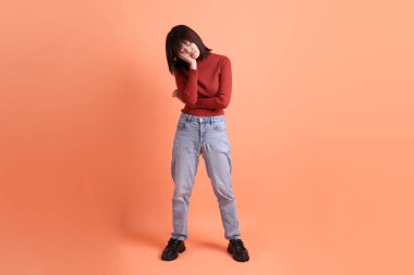 Kırmızı uzun kollu tişörtlü kısa saçlı Asyalı kadın. Turuncu arka planda duran ve gülümseyen. Gen Z