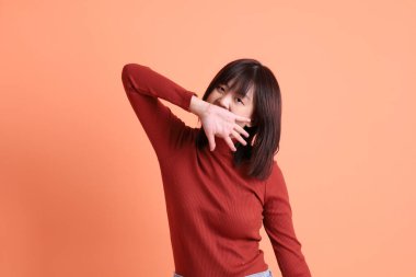 Kırmızı uzun kollu tişörtlü kısa saçlı Asyalı kadın. Turuncu arka planda duran ve gülümseyen. Gen Z