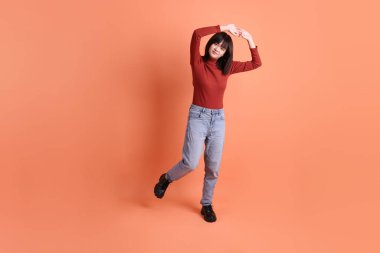 Kırmızı uzun kollu tişörtlü kısa saçlı Asyalı kadın. Turuncu arka planda duran ve gülümseyen. Gen Z