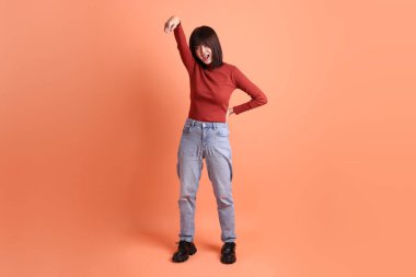 Kırmızı uzun kollu tişörtlü kısa saçlı Asyalı kadın. Turuncu arka planda izole edilmiş öfkeli ve çığlıklar atan bir jest. Gen Z