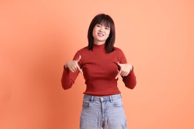 Kırmızı uzun kollu tişörtlü kısa saçlı Asyalı kadın turuncu arka planda izole edilmiş bir işaret hareketi yapıyor. Gen Z