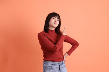 Kırmızı uzun kollu tişörtlü kısa saçlı Asyalı kadın turuncu arka planda izole edilmiş bir işaret hareketi yapıyor. Gen Z