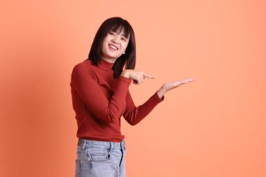 Kırmızı uzun kollu tişörtlü kısa saçlı Asyalı kadın turuncu arka planda izole edilmiş bir işaret hareketi yapıyor. Gen Z