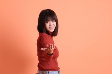Kırmızı uzun kollu tişörtlü kısa saçlı Asyalı kadın turuncu arka planda izole edilmiş bir işaret hareketi yapıyor. Gen Z