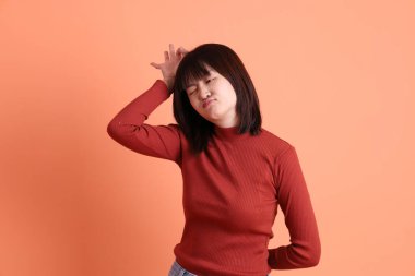 Kırmızı uzun kollu tişörtlü kısa saçlı Asyalı kadın başparmak hareketi yapıyor ya da turuncu arka planda izole olduğunu onaylıyor. Gen Z