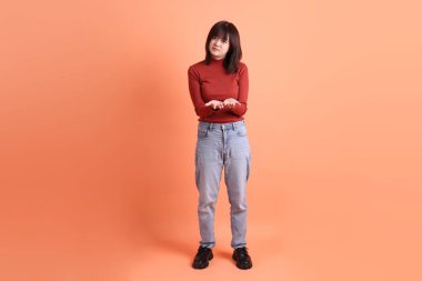 Kırmızı, uzun kollu tişörtlü kısa saçlı Asyalı kadın turuncu arka planda izole edilmiş bir jest yapıp alıyor. Gen Z