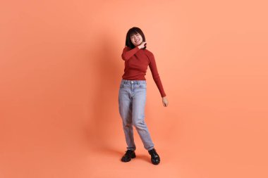 Kırmızı uzun kollu tişörtlü kısa saçlı Asyalı kadın. Turuncu arka planda duran ve gülümseyen. Gen Z