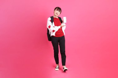 Kırmızı tişörtlü Asyalı kız öğrenci ya da günlük kıyafetler, kırmızı kalp şeklinde gömlek okul çantası taşıyor ve pembe arka planda Holding cep telefonu var. Gen Z