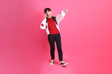 Kırmızı tişörtlü Asyalı kız öğrenci ya da günlük kıyafetler, kırmızı kalp şeklinde gömlek okul çantası taşıyor ve pembe arka planda Holding cep telefonu var. Gen Z