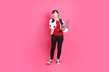 Kırmızı tişörtlü Asyalı kız öğrenci ya da günlük kıyafetler, kırmızı kalp şeklinde gömlek, pembe arka planda tutulan dizüstü bilgisayarın jesti ile okul çantası taşıyor. Gen Z