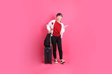 Kırmızı tişörtlü Asyalı kız öğrenci ya da günlük kıyafetler, kırmızı kalp şeklinde gömlek okul çantası taşıyor ve pembe arka planda izole edilmiş bir çanta taşıyor. Gen Z, yurtdışında eğitim