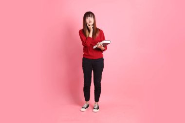 Kırmızı tişörtlü Asyalı kız öğrenci ya da günlük kıyafetler içinde pembe arka planda izole edilmiş düşünce jestleriyle okul çantası ve kitap taşıyorlar. Gen Z
