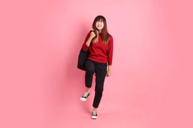 Kırmızı tişörtlü Asyalı kız öğrenci ya da günlük kıyafetler içinde okul çantası ve evet jestli kitaplar taşıyorlar, heyecanlı, pembe arka planda izole edilmiş kutlamayı kutluyorlar. Gen Z