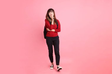 Kırmızı tişörtlü Asyalı kız öğrenci ya da günlük kıyafetler içinde pembe arka planda izole edilmiş düşünce jestleriyle okul çantası ve kitap taşıyorlar. Gen Z