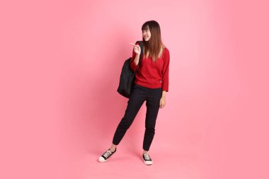 Kırmızı tişörtlü Asyalı kız öğrenci ya da günlük giysiler içinde okul çantası ve pembe arka planda izole edilmiş işaret eden kitaplar taşıyorlar. Gen Z