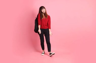 Kırmızı tişörtlü ya da sıradan giysili Asyalı kız öğrenci pembe arka planda okul çantası taşıyor. Gen Z