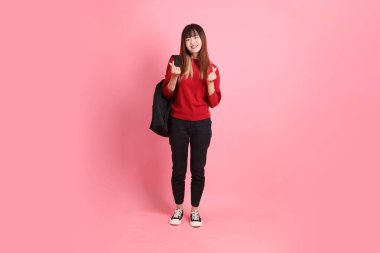 Kırmızı tişörtlü Asyalı kız öğrenci ya da günlük kıyafetler içinde okul çantası taşıyorlar. Kalp şeklinde bir jest, küçük kalp, pembe arka planda izole edilmiş aşk. Gen Z