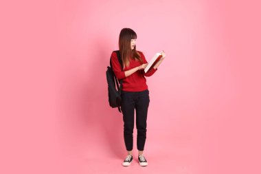 Kırmızı tişörtlü Asyalı kız öğrenci ya da günlük kıyafetler okul çantası ve pembe arka planda sıralanmış kitaplar taşıyor. Gen Z