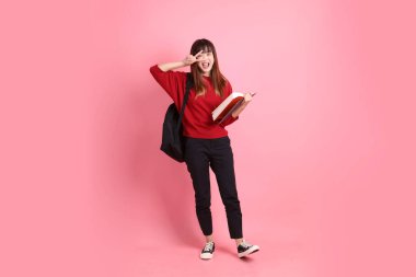 Kırmızı tişörtlü Asyalı kız öğrenci ya da günlük kıyafetler okul çantası ve pembe arka planda sıralanmış kitaplar taşıyor. Gen Z