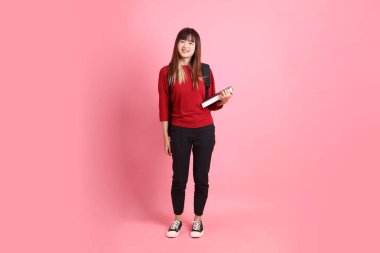 Kırmızı tişörtlü Asyalı kız öğrenci ya da günlük kıyafetler okul çantası ve pembe arka planda sıralanmış kitaplar taşıyor. Gen Z