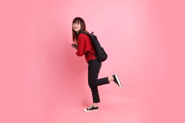 Kırmızı tişörtlü Asyalı kız öğrenci ya da günlük kıyafetler okul çantası ve pembe arka planda sıralanmış kitaplar taşıyor. Gen Z