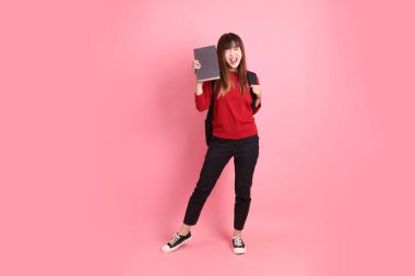 Kırmızı tişörtlü Asyalı kız öğrenci ya da günlük kıyafetler içinde okul çantası ve evet jestli kitaplar taşıyorlar, heyecanlı, pembe arka planda izole edilmiş kutlamayı kutluyorlar. Gen Z