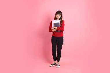 Kırmızı tişörtlü Asyalı kız öğrenci ya da günlük kıyafetler okul çantası ve pembe arka planda sıralanmış kitaplar taşıyor. Gen Z