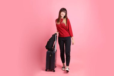 Kırmızı tişörtlü Asyalı kız öğrenci ya da günlük giysiler içinde okul çantası ve bavulu pembe arka planda tek başına taşıyor. Gen Z