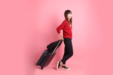 Kırmızı tişörtlü Asyalı kız öğrenci ya da günlük giysiler içinde okul çantası ve bavulu pembe arka planda tek başına taşıyor. Gen Z
