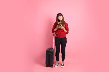 Kırmızı tişörtlü Asyalı kız öğrenci ya da günlük kıyafetler içinde okul çantası ve pembe arka planda izole edilmiş bir bavul taşıyorlar. Gen Z
