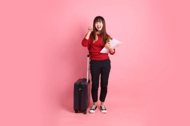 Kırmızı tişörtlü Asyalı kız öğrenci ya da günlük giysiler içinde okul çantası ve pembe arka planda izole edilmiş bir işaret işareti içeren bavul taşıyorlar. Gen Z